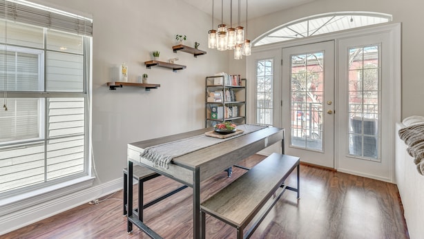 A modern kitchen with a central island, wooden flooring, and a built-in bench. There are floating shelves with plants and books, and a chandelier hangs above. - Walkable Dtwn Fort Walton Beach Condo w/ Balcony! (Fort Walton Beach)