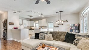 A spacious living room with a large sofa, a coffee table with a tray, and a bookshelf filled with books. - Walkable Dtwn Fort Walton Beach Condo w/ Balcony! (Fort Walton Beach)