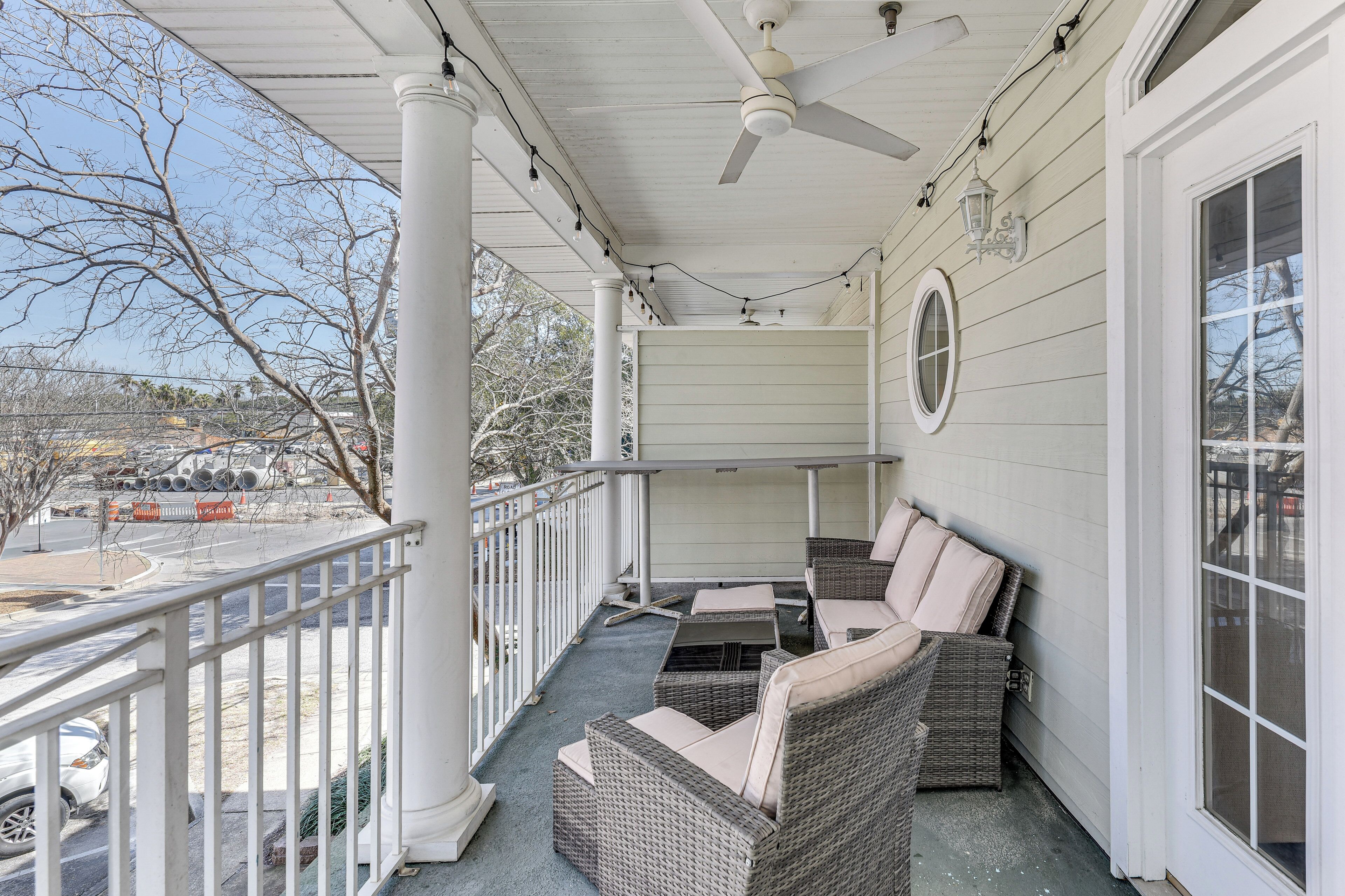 A covered porch with wicker furniture, a ceiling fan, and a view of a parking lot and trees.