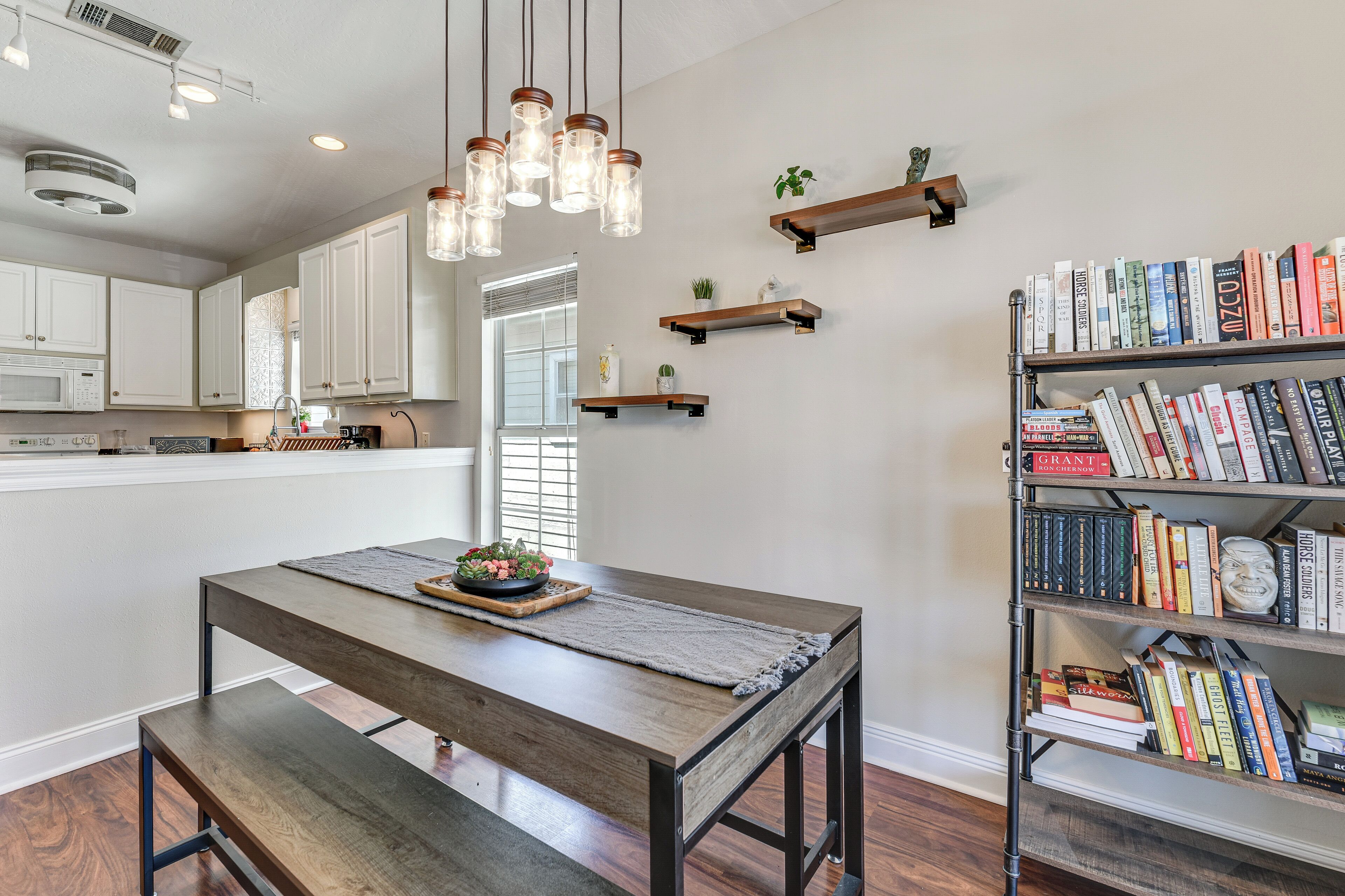 A modern kitchen with white cabinets, a wooden dining table, and a bookshelf filled with books.