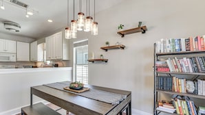 A modern kitchen with white cabinets, a wooden dining table, and a bookshelf filled with books. - Walkable Dtwn Fort Walton Beach Condo w/ Balcony! (Fort Walton Beach)