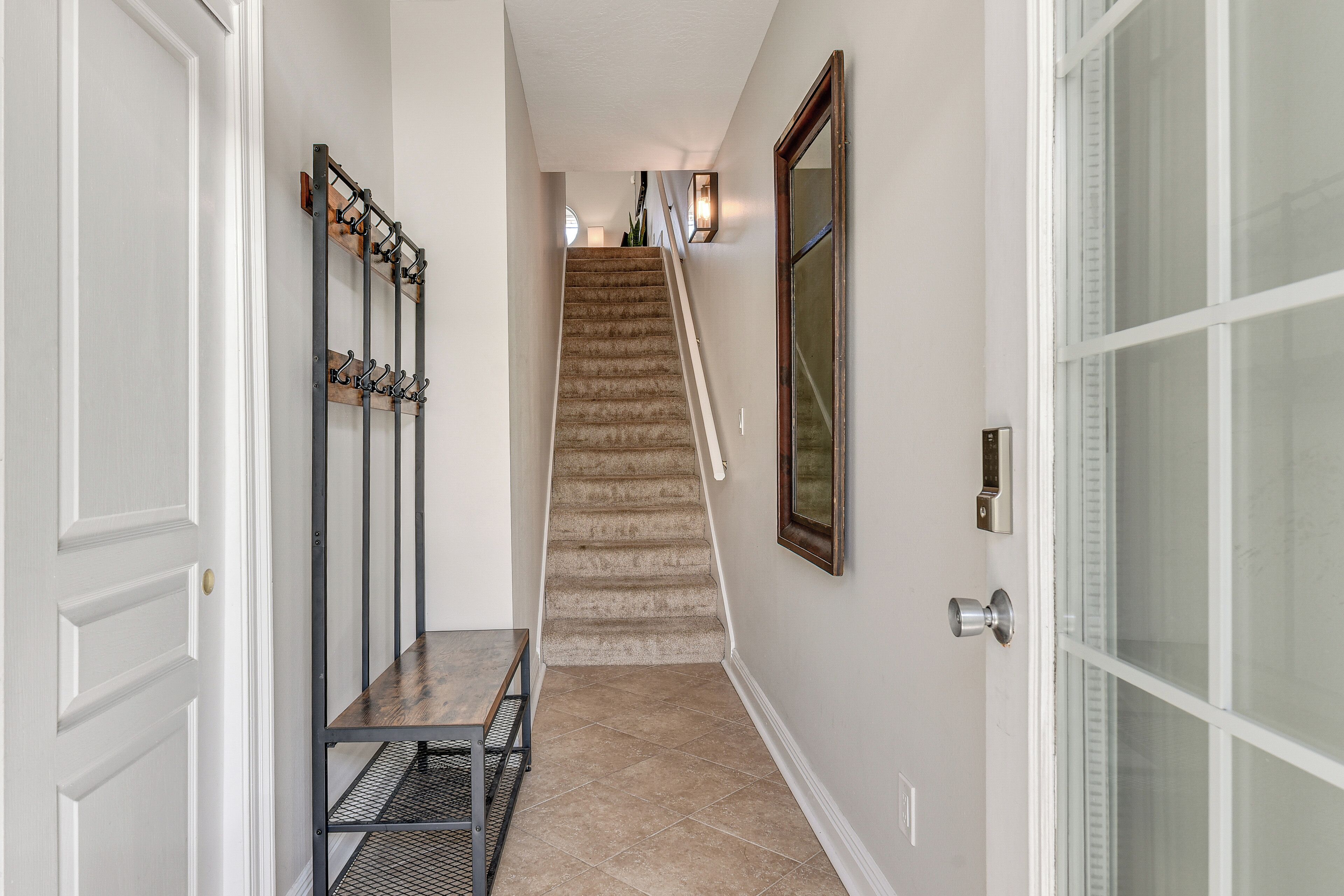 A hallway with a staircase, a coat rack, and a door with a glass panel.