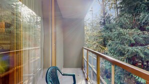 Un balcon donnant sur une forêt dense, une chaise et un mur de verre qui reflète le paysage extérieur.