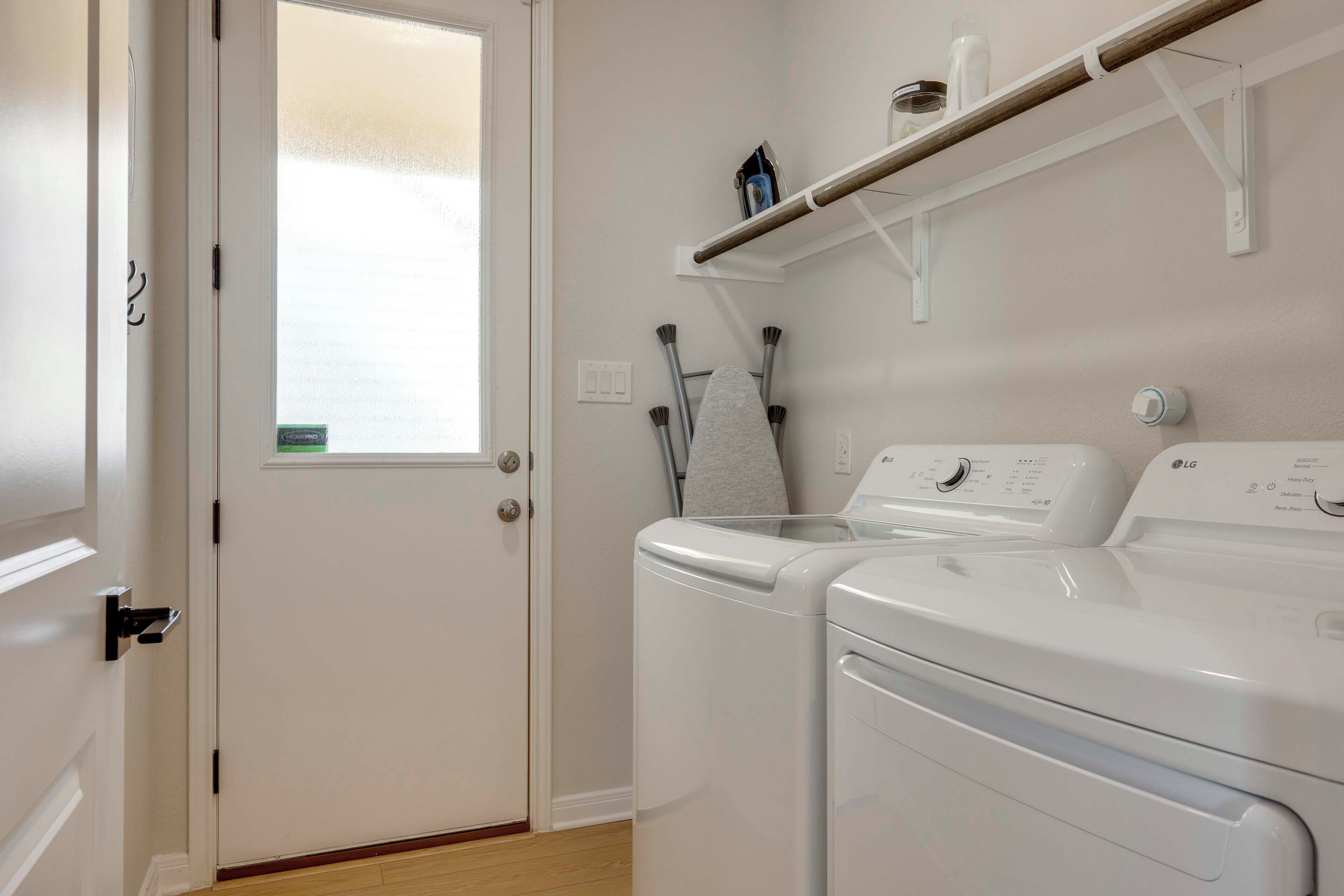 A laundry room with two stacked front-loading washing machines, a drying rack, and a window with frosted glass.
