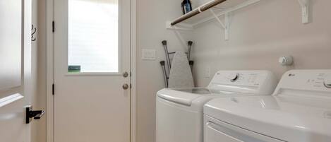 A laundry room with two stacked front-loading washing machines, a drying rack, and a window with frosted glass.