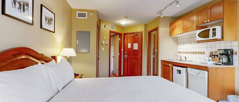A hotel room with a bed, a desk, a microwave, and a small kitchenette.