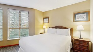 Hotelkamer met een groot bed, twee nachtkastjes met lampen, een raam met jaloezieën en twee ingelijste foto's aan de muur.