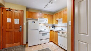 A compact kitchen with wooden cabinets, a refrigerator, stove, microwave, and dishwasher. - Whistler - Cascade Lodge 433 (Whistler)