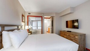 Une chambre d’hôtel avec un grand lit, une tête de lit en bois, un téléviseur fixé au mur et une commode en bois.