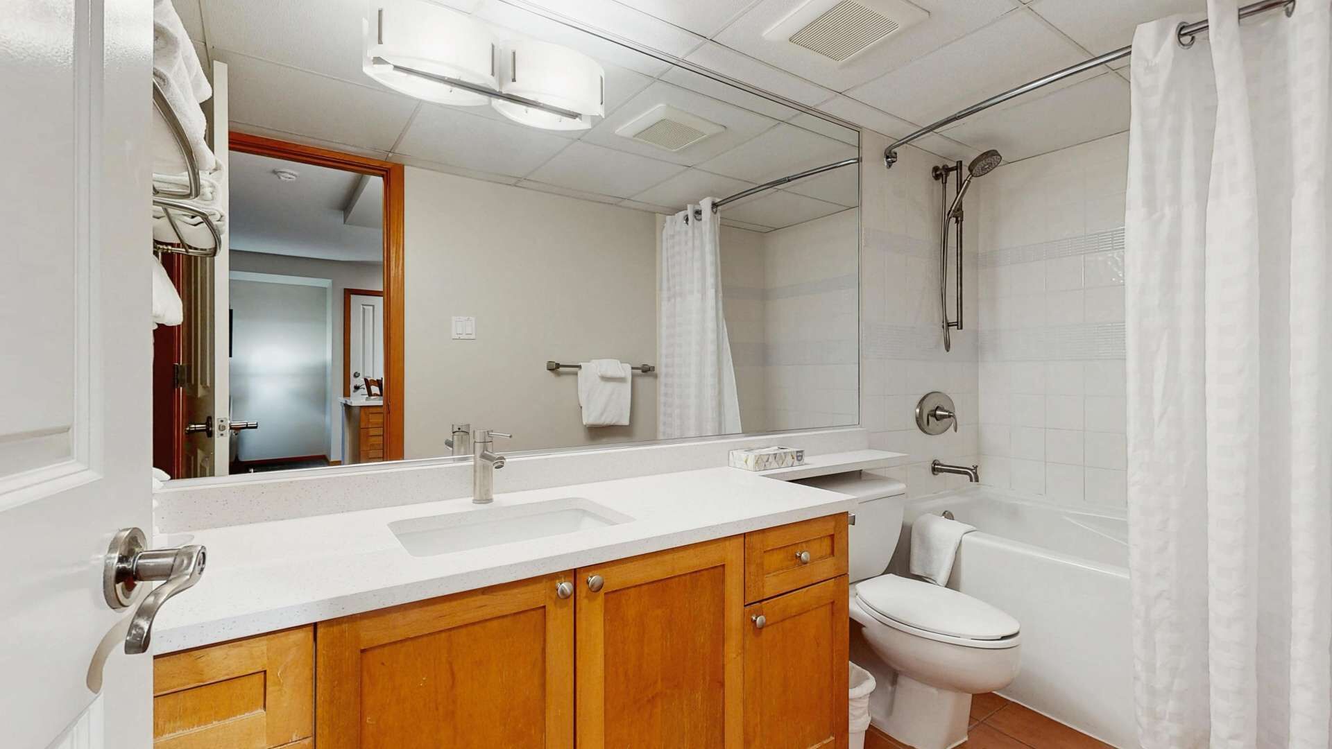 Un baño con lavamanos blanco, armarios de madera, un espejo, inodoro y zona de ducha.