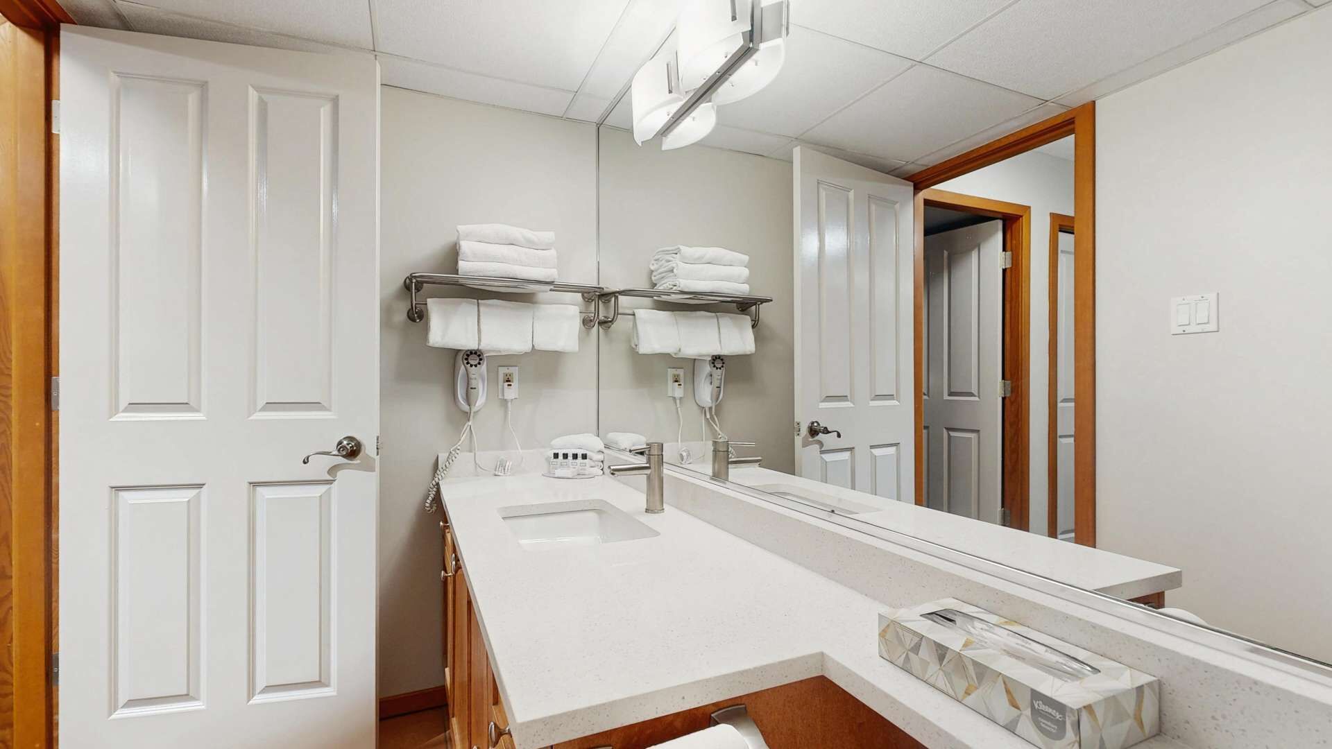 A hotel bathroom with a large mirror, two towel racks, a sink, and a shower area.