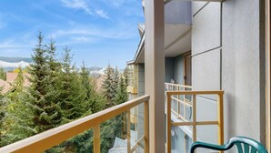 Un balcon offrant une vue sur des arbres à feuilles persistantes et un ciel dégagé.