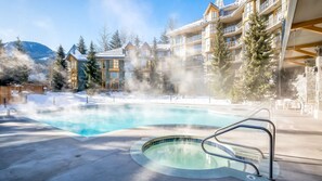 Un jacuzzi rodeado por una piscina, con un edificio al fondo.