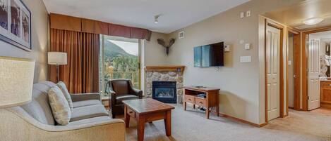 A living room with a sofa, armchair, coffee table, fireplace, TV, and a view of the outdoors.