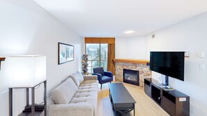 Un salon moderne avec un canapé, un fauteuil bleu, une cheminée et un téléviseur.