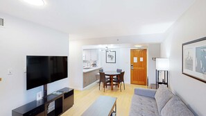 A modern living room with a flat-screen TV, a sofa, a coffee table, and a dining area with a wooden table and chairs.