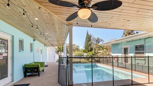 Ein überdachter Außenbereich mit Pool, Deckenventilator und grünem Sofa.