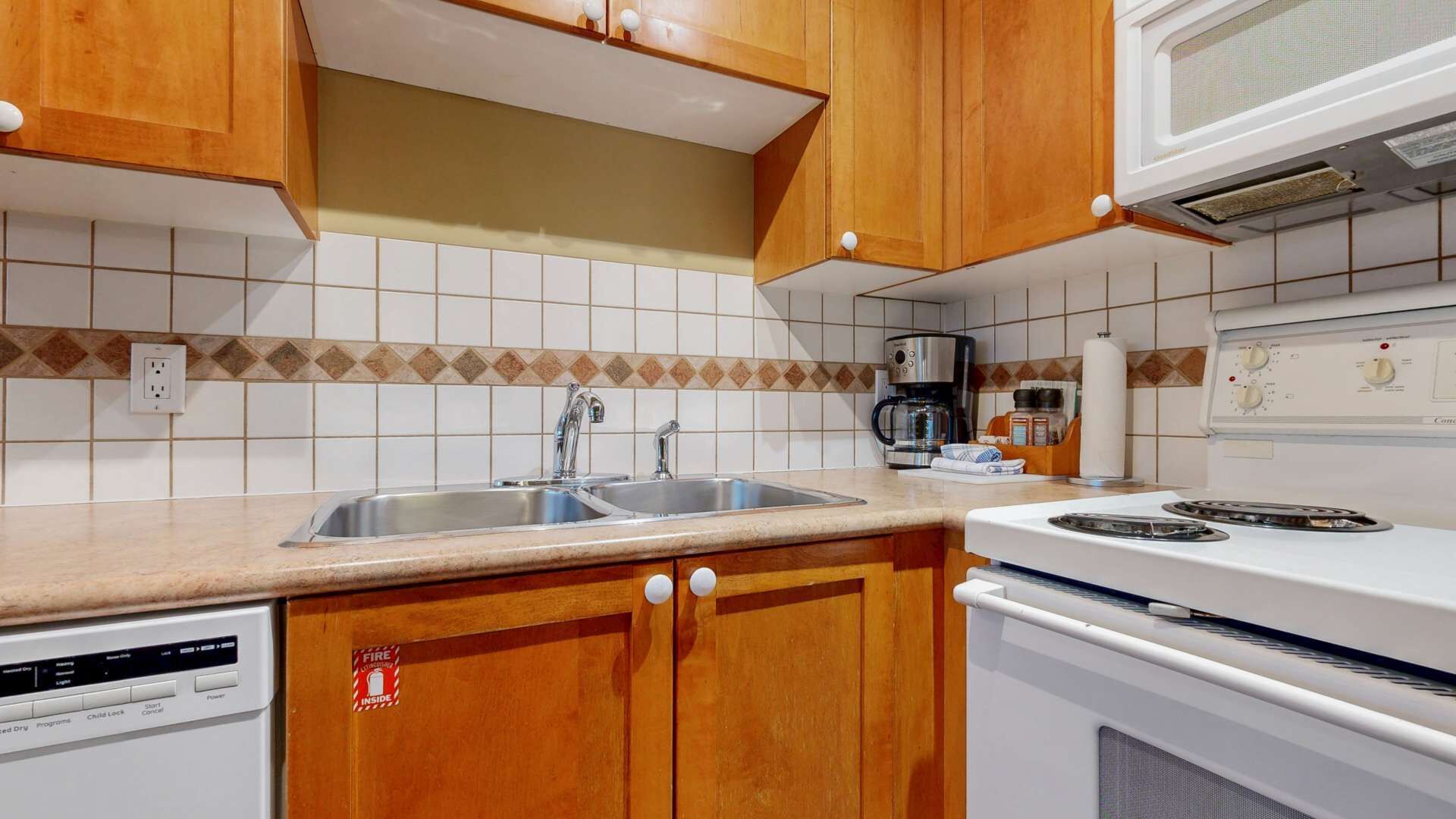 Une cuisine avec des meubles de rangement en bois, un évier à deux bacs, une machine à café et une cuisinière.
