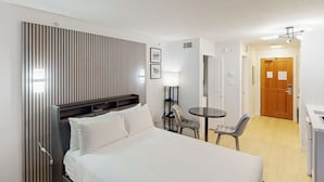 Une chambre d’hôtel avec un lit, un bureau, une chaise, une lampe et une porte.