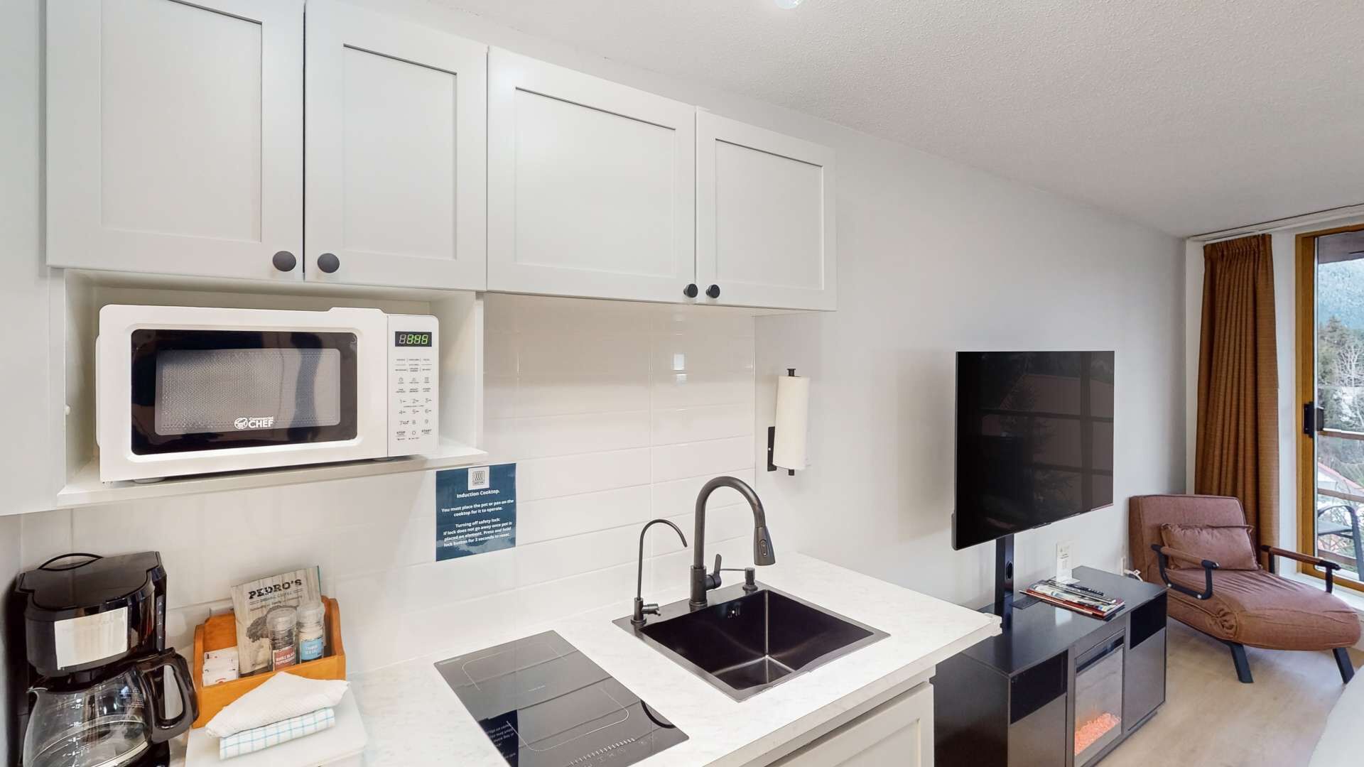 A compact kitchen with white cabinets, a microwave, a sink, and a coffee maker.