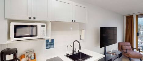 A compact kitchen with white cabinets, a microwave, a sink, and a coffee maker.