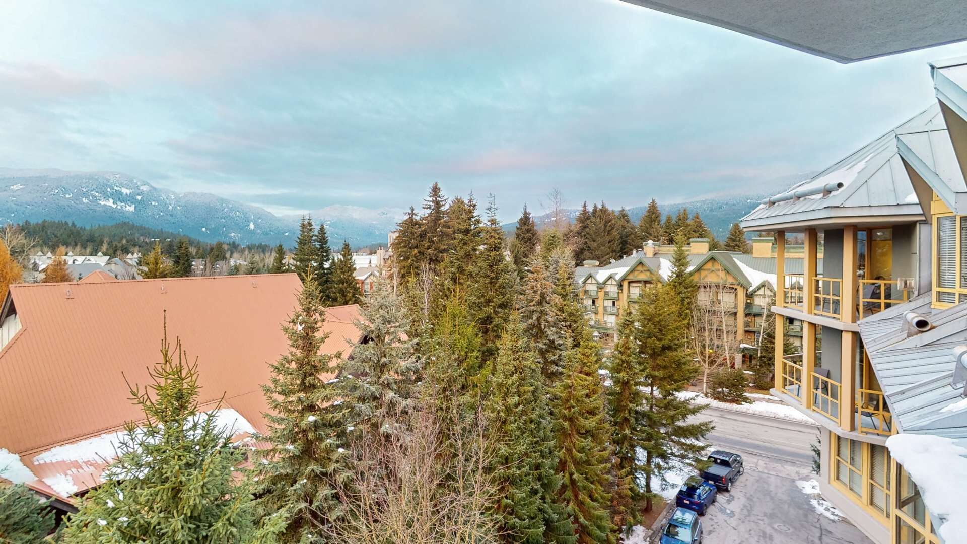 Un hotel con diversi piani, un'area di parcheggio e vista sulle montagne e sugli alberi.