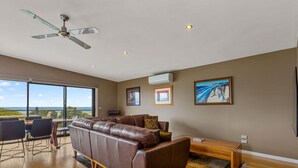 A spacious living room with a large window, a ceiling fan, and a view of the outdoors. - Achilles (Apollo Bay)