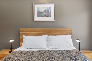 A neatly made bed with white linens, a patterned bedspread, and a framed artwork above it. - Achilles (Apollo Bay)