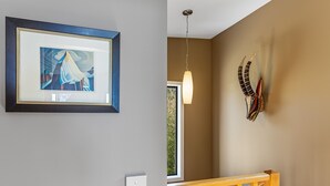 A room with a framed artwork on the wall, a pendant light, and a decorative headpiece. - Achilles (Apollo Bay)