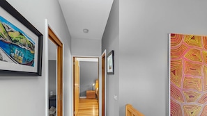 A hallway with a wooden floor, a door leading to a room, and a colorful abstract painting on the wall. - Achilles (Apollo Bay)