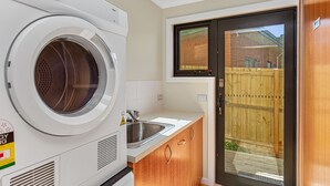 A compact laundry room with a front-loading washer and dryer, a sink, and a door leading to an outdoor area. - Achilles (Apollo Bay)