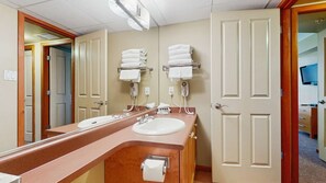 Een hotelbadkamer met twee wastafels, een spiegel, handdoekrekken en een haardroger.