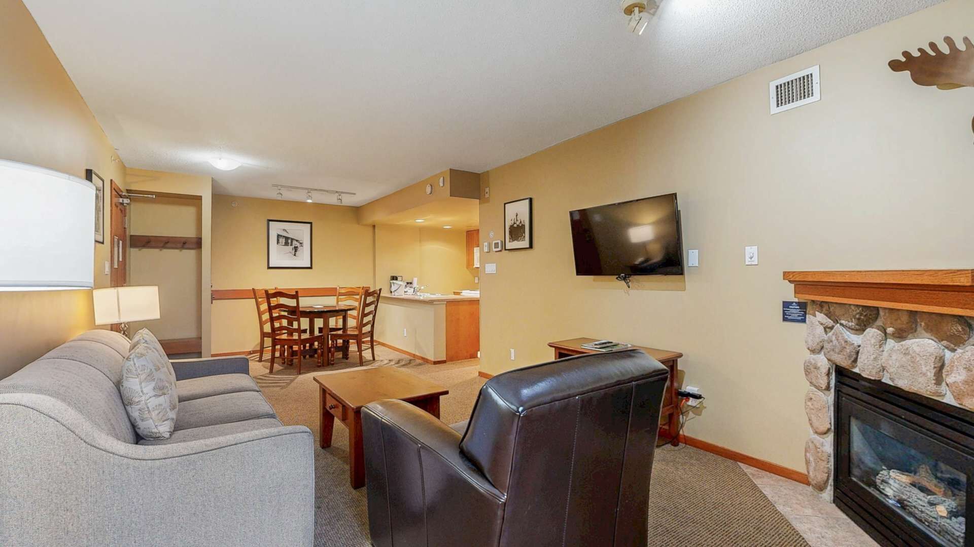 Een woonkamer met een bank, een lederen fauteuil, een televisie en een open haard.