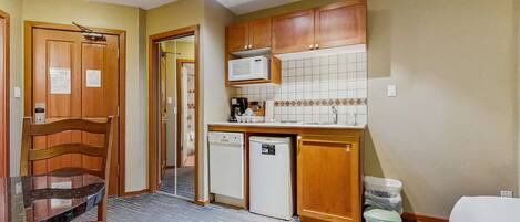 A compact kitchen with wooden cabinets, a microwave, a dishwasher, and a sink.