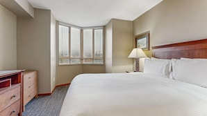 Une chambre d’hôtel avec un grand lit, un bureau avec des tiroirs, une lampe et une fenêtre avec des stores.