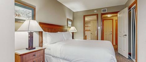 A hotel room with a large bed, two bedside tables with lamps, a wooden headboard, and a door leading to a bathroom.