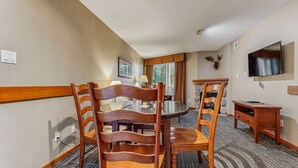 Ein Hotel-Essbereich mit rundem Tisch, Holzsesseln, einem Steinkamin und einem an der Wand befestigten Fernseher.