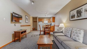 Ein kompaktes Hotelzimmer mit Küchenzeile, Essecke, einer Couch und einem an der Wand befestigten Fernseher.