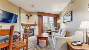 Ein Wohnzimmer mit Kamin aus Stein, einem Fernseher, einer Couch, einem Sessel, einer Lampe und einem Telefon.