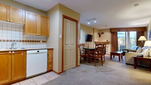 Eine kompakte Küche mit Holzschränken und einem Geschirrspüler, ein Essbereich mit Tisch und Stühlen sowie ein Wohnzimmer mit Sofa und Fernseher.