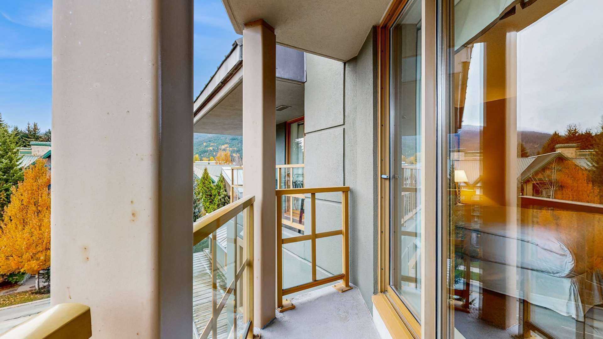 A balcony with a glass door, a wooden railing, and a view of a residential area with trees and houses.