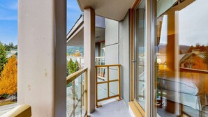Ein Balkon mit Glasdoor, Holzbalkon und Blick auf eine Wohngegend mit Bäumen und Häusern.