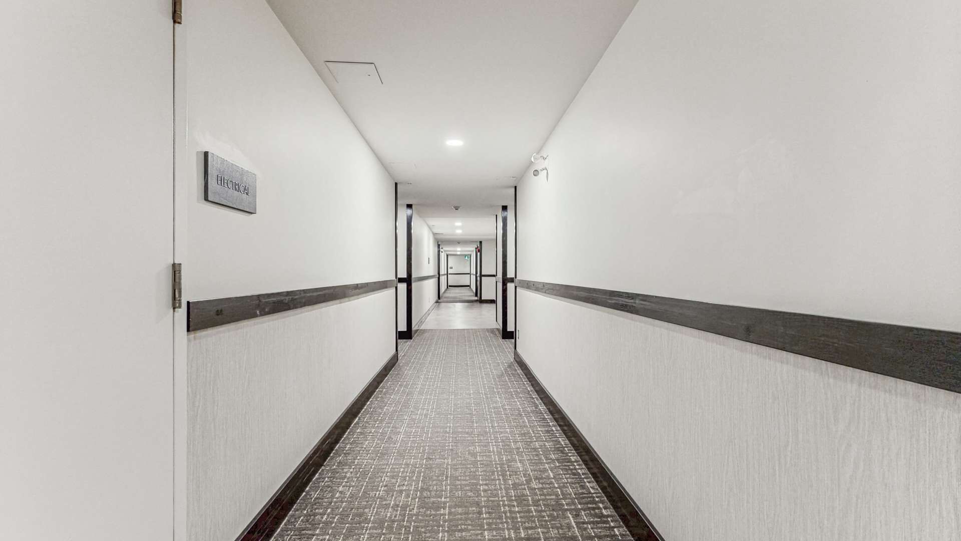 En lang, smal hotelgang med flisegulv og et skilt, der angiver et elrum.