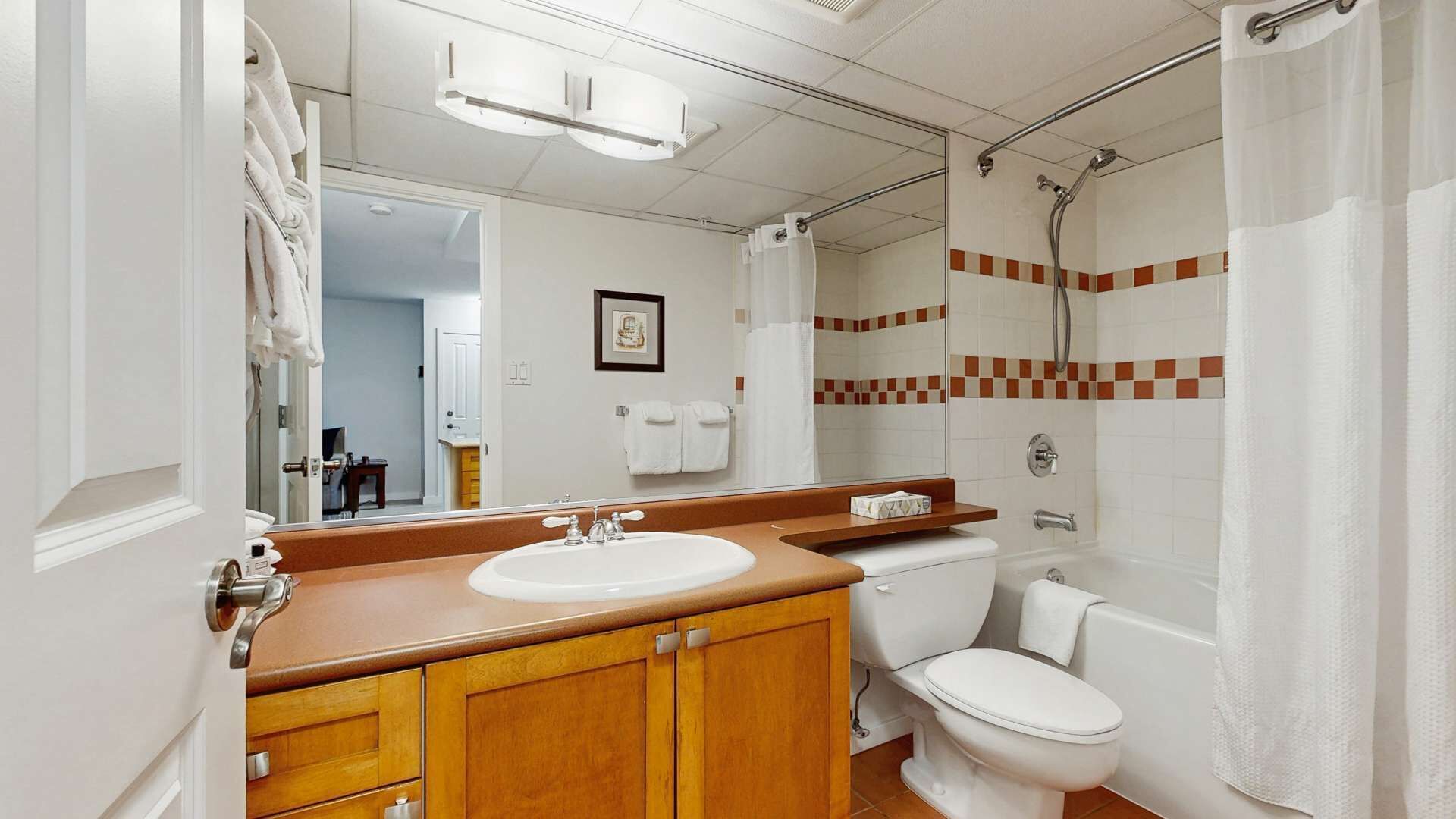 Un baño con tocador de madera, lavamanos blanco, inodoro y ducha con puerta de vidrio.