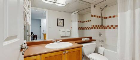 Un baño con tocador de madera, lavamanos blanco, inodoro y ducha con puerta de vidrio.