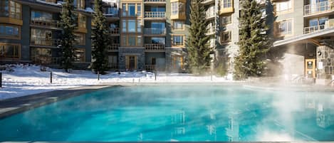 Uma piscina interior ampla com superfície de água azul cristalina, rodeada por edifícios de vários andares com varandas e janelas grandes.
