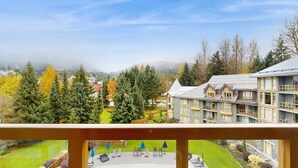 Ein mehrstöckiges Gebäude mit Balkonen, umgeben von Bäumen und Blick auf eine Berglandschaft.