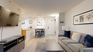 Ein modernes Wohnzimmer mit einer Couch, einem Fernseher, einem Couchtisch und einem Essbereich mit Stühlen und Tisch.
