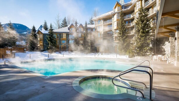 A hot tub surrounded by a pool, with a building featuring balconies and a snowy landscape in the background. - Whistler - Cascade Lodge 508 (Whistler)