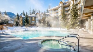 A hot tub surrounded by a pool, with a building featuring balconies and a snowy landscape in the background. - Whistler - Cascade Lodge 633 (Whistler)